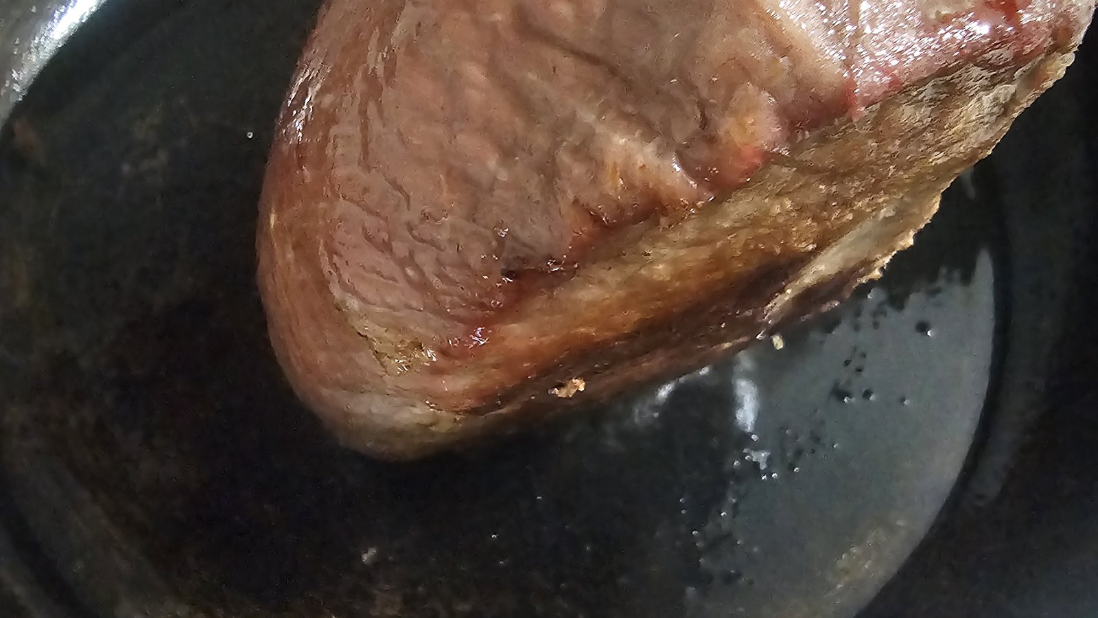 A beef roast searing in a cast-iron pan.